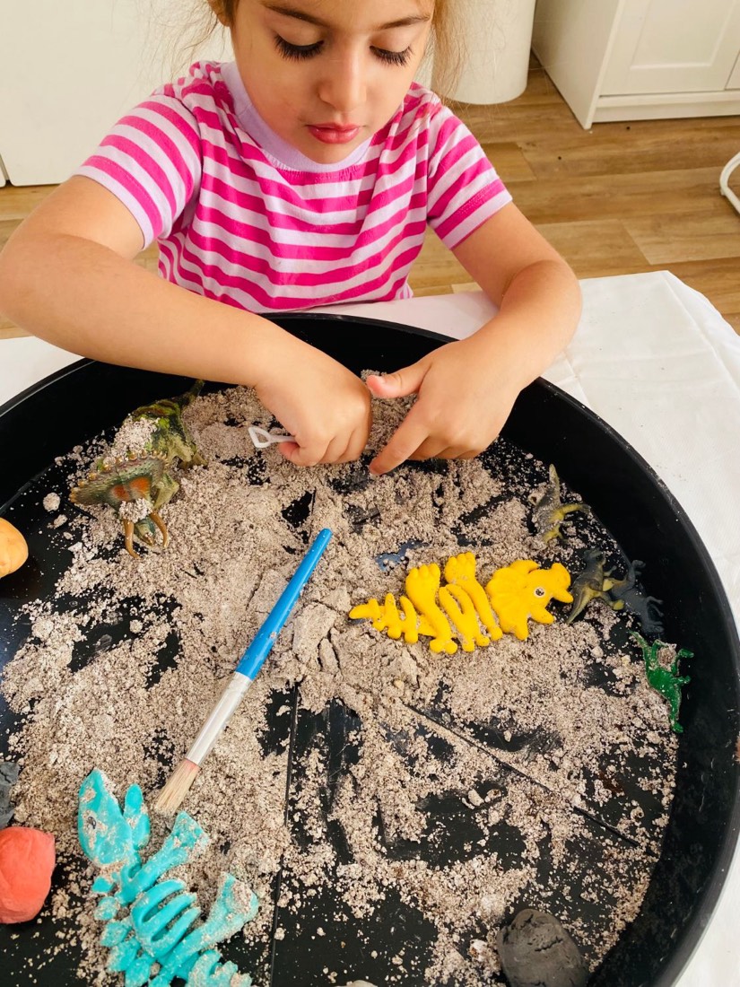Girl digging for dinosaur fossils in a sensory tray