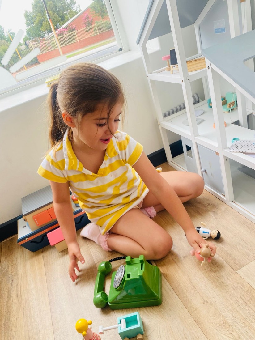 Girl playing with the dolls house and a toy phone by the window