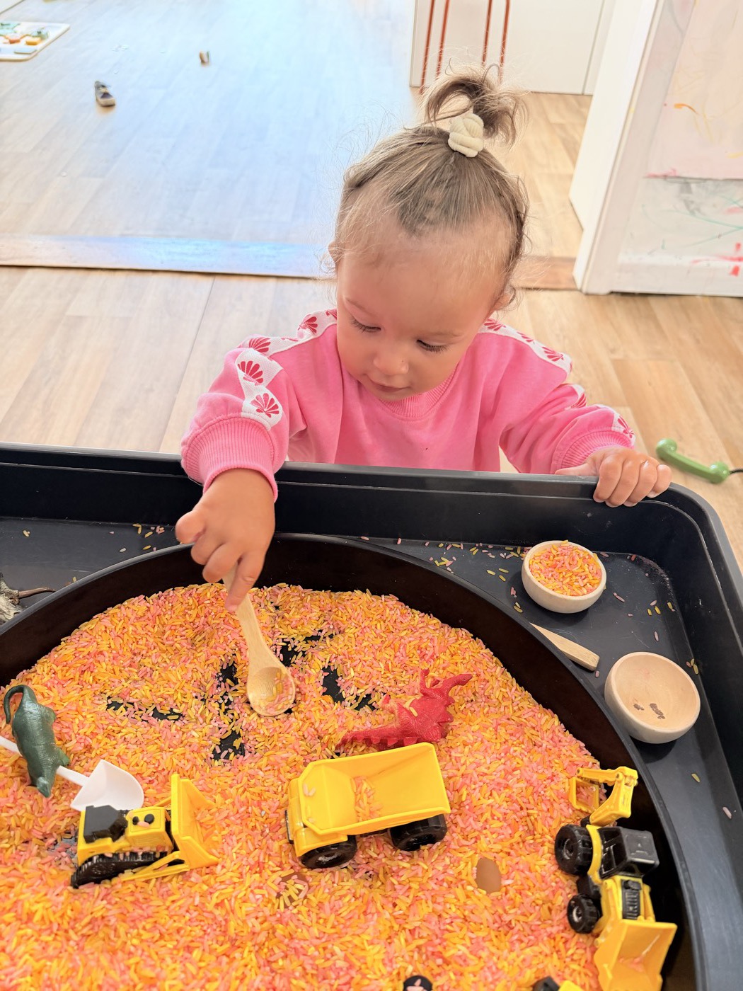 Girl scooping coloured rice with toy diggers