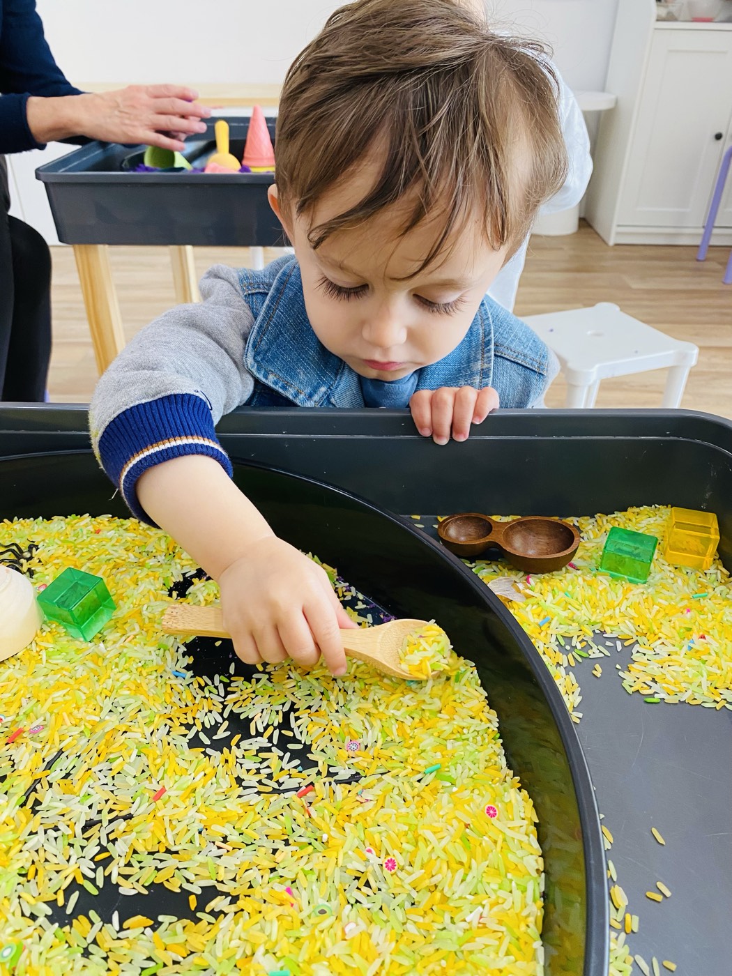 Toddler scooping rice in a sensory tray